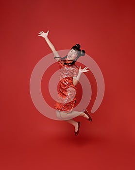 Happy Chinese new year. Happy smiling children asian girl wearing traditional qipao dress jumping celebrate isolated on red