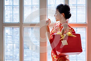 Happy chinese woman wearing a qipao dress traditional or cheongsam hand holding gift bags near window at home