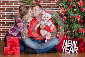 Happy Christmas Family portrait. Smiling Parents with baby daughter at Home Celebrating New Year. Christmas Tree