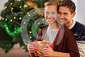 Happy, Christmas gift and portrait of couple in living room at home for festive celebration. Smile, love and young man