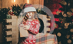 Happy Christmas little girl is opening a Christmas gift. Beautiful little girl wearing Santa hat. Christmas time. Happy