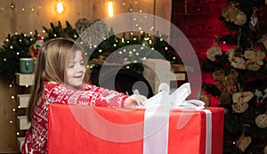 Happy Christmas little girl wants to open a big Christmas present. Beautiful little girl wearing red sweater. Christmas