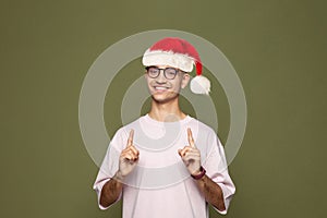 Happy Christmas man Santa wearing blank t-shirt pointing up on green studio wall background