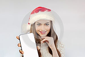 Happy Christmas woman in red Santa hat smiling and holding smartphone with empty white screen display