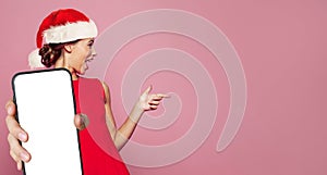 Happy Christmas woman Santa showing smartphone with blank empty screen display and pointing finger aside