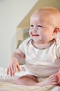 Happy chubby baby sitting on bed