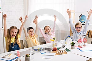 Happy classmates rejoicing with raised hands after STEM class