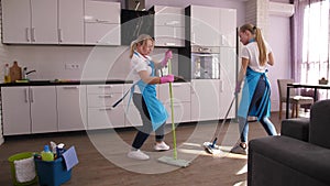 Happy cleaning ladies dancing while mopping floor