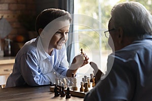 Happy clever grandson beating grandpa in chess battle