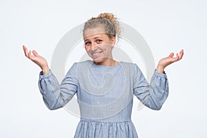 Happy clueless young woman in dress shrugging with hands spread aside smiling.