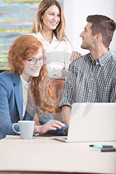 Happy co-workers gathering around laptop