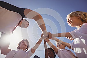 Happy coach and schoolkids forming handstack