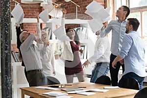 Happy colleagues celebrating successful project accomplishment throwing papers up