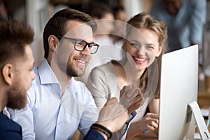 Happy colleagues looking at computer screen talking laughing working together