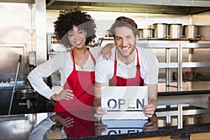 Happy colleagues posing with open sign