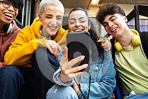 Happy college student friends look mobile phone laughing together. Multiracial teenagers using smartphone outside.