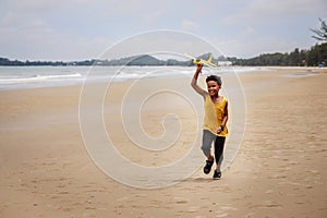 Happy colored boy and African American boy playing yellow toy airplane and running by wearing yellow sweater. Having fun on beach