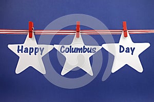 Happy Columbus Day message greeting written across white star cards hanging from red stripes ribbon and pegs on a line