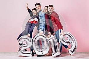 Happy company of two girls and two guys dressed in stylish clothes are holding balloons in the shape of numbers 2019 on