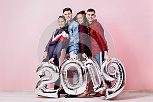 Happy company of two girls and two guys dressed in stylish clothes are holding balloons in the shape of numbers 2019 on