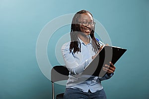 Happy confident african american woman with clipboard documentation signing agreement papers on blue background.