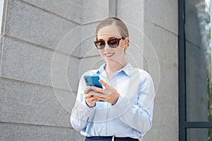 happy confident business woman typing on phone stand in city