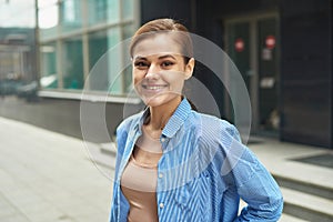 Happy confident business woman walking out of modern office center. Portrait of successful enterpreneur in smart casual