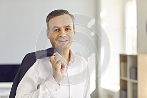 Happy confident businessman standing on office, holding jacket over shoulder and looking at camera