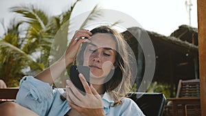 Happy confident businesswoman sitting in beach lounge chair using smartphone mobile office app on vacation resort.