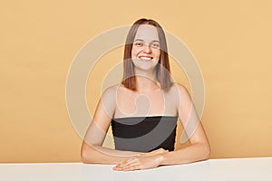 Happy confident cheerful young happy woman wearing black top looking at camera being in good mood sitting at table posing 