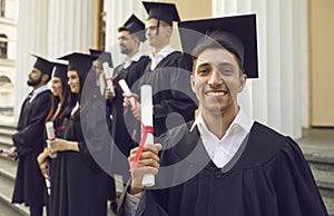 Happy confident graduate guy in a mantle with a diploma in his hands.