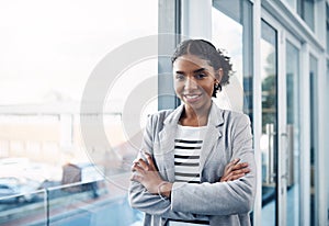 Happy, confident and professional young business woman folding her arms while standing in a modern office. Portrait of a