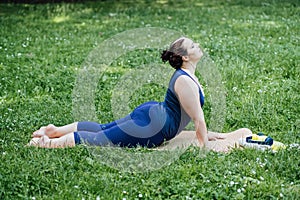 Happy confident smiling plus size curvy woman doing yoga stretching pilates workout, exercising outdoors.