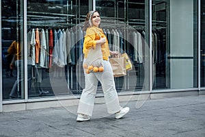 Happy confident smiling plus size curvy young woman with shopping bags walking on city street near shop windows