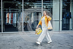 Happy confident smiling plus size curvy young woman with shopping bags walking on city street near shop windows