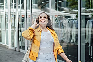 Happy confident smiling plus size curvy young woman with shopping bags walking on city street near shop windows
