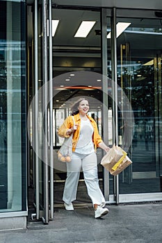 Happy confident smiling plus size curvy young woman with shopping bags walking on city street near shop windows