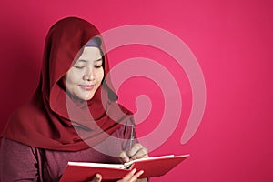 Happy confident successful Asian muslim woman wearing hijab  writing on book, smiling and thinking