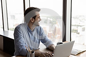 Happy confident thoughtful businessman using laptop, looking out office window