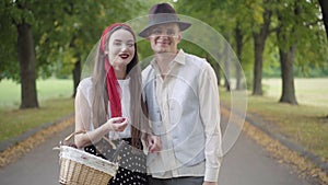 Happy confident young couple in elegant outfit standing on park alley talking, looking at camera and smiling. Portrait