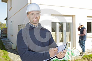 Happy construction inspector on building site writing on clipboard