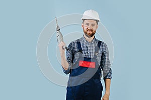 Happy construction worker in a white helmet and blue overalls with a hand drill