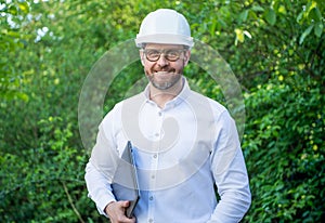 Happy constructor man in hardhat holding laptop outdoors