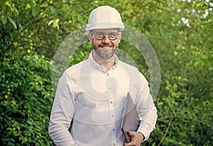 Happy constructor man in hardhat holding laptop outdoors