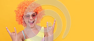 happy cool teen girl in sunglasses wearing orange curly wig hair on yellow background, childhood. Funny teenager child
