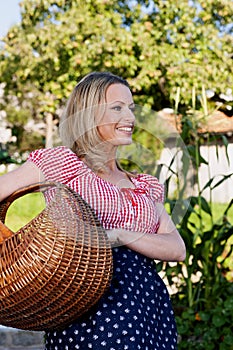 Happy countrywoman with a basket with carrots in her garden