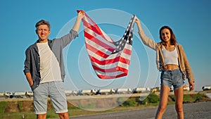 happy couple, american family standing on road at sunset and holding flag of USA with proud on wind, celebration fourth