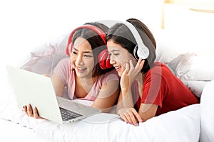 Happy Couple  asia woman wear headphones and enjoy musics playing mobile phone and tablet in bedroom