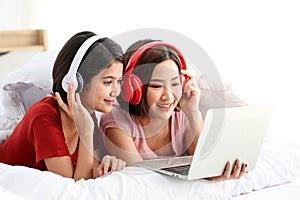 Happy Couple  asia woman wear headphones and enjoy musics playing mobile phone and tablet in bedroom