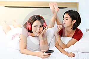 Happy Couple  asia woman wear headphones and enjoy musics playing mobile phone and tablet in bedroom